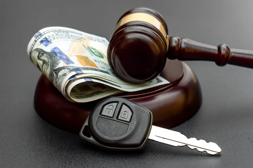 Closeup shot of a gavel, car keys, and a stack of dollar bills